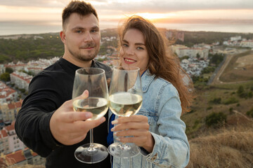 Loving couple clinking glasses of white wine at sunset on a hilltop