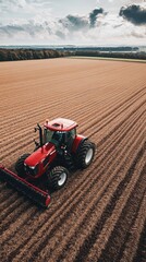 Obraz premium A tractor plows through a vast, brown field under a cloudy sky
