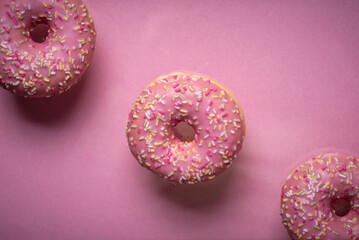 Close-up of three pink sprinkled donuts on bright pink background, tasty treats.