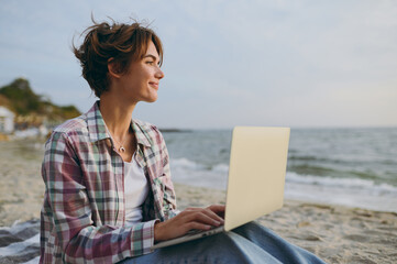 Side view young IT woman wear shirt casual clothes hold use work on laptop pc computer look aside...