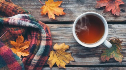 A steaming cup of tea sits on a rustic wooden table surrounded by vibrant autumn leaves and a cozy blanket.