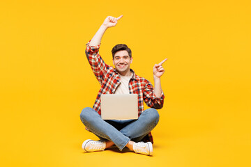 Full body young fun happy IT man he wears red checkered shirt casual clothes sits hold use work on...