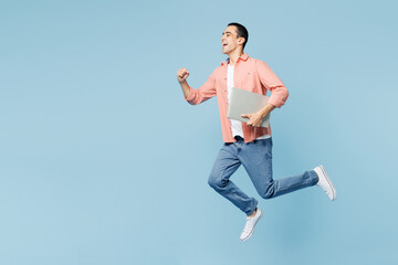 Full body young smart IT middle eastern man he wearing pink shirt white t-shirt jump high hold closed laptop pc computer isolated on plain pastel light blue cyan background studio. Lifestyle concept. © ViDi Studio