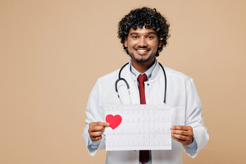 Young doctor man wears white gown suit work in hospital clinic office hold electrocardiogram record, heart ekg cardiogram chart of wave in paper isolated on plain beige background. Healthcare concept.