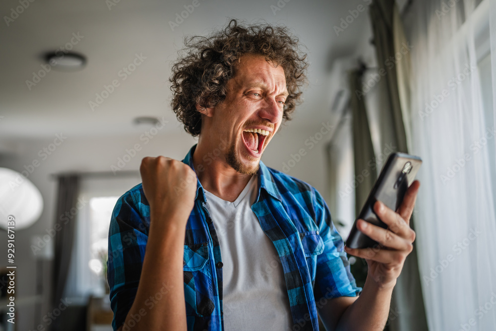 Wall mural excited adult caucasian man use mobile phone and do winner gesture