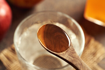 Apple cider vinegar on a wooden spoon above a glass of water