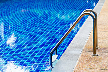 Bright blue tiled swimming pool with stainless steel ladder, leading into water, creating...