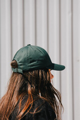 A profile view of a woman wearing a green cap. The light, subtle blur, and graininess focus attention on her relaxed posture, creating a minimalist yet visually compelling image.