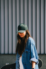 A young woman in a green cap and denim jacket, captured in a candid moment with a skateboard. The graininess and blur add a gritty, urban artistic effect to the photograph.