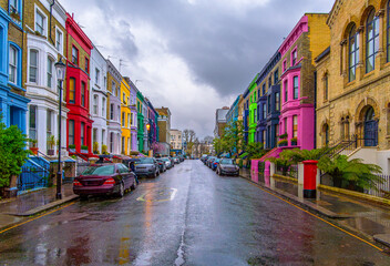 Obraz premium View of the wonderful Lancaster Road, the mythical street of colorful houses under a fine rain with a cloudy sky and pedestrians walking with umbrellas in Notting Hill, London, England.