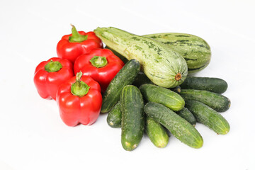Fresh red bell peppers. Green cucumbers. Zucchini arranged on a white background. Vibrant vegetables. Variety of colors and textures. Healthy produce perfect for salads and cooking.
