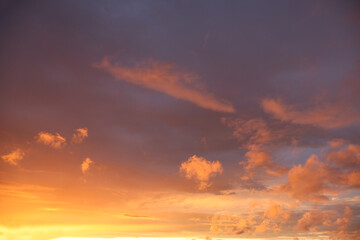 A sunset over the horizon, with delicate shades of orange and bluish, as the sun dips below the horizon. Clouds create serenity and drama to the scene.