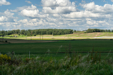 Thick clouds over green fields. The highway is far beyond the field