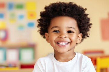 smiling little black boy sitting at the table with, kindergarten classroom in the background