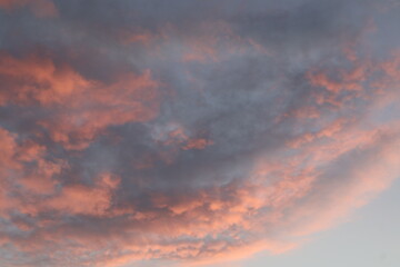 A sunset over the horizon, with delicate shades of pink and purple, as the sun dips below the horizon. Clouds create serenity and drama to the scene.