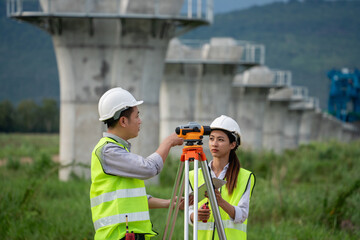 Survey team is working with a theodolite and road construction plans. Civil engineers are taking measurements with surveying tools during the construction.