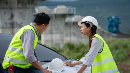 Survey team is working with a theodolite and road construction plans. Civil engineers are taking measurements with surveying tools during the construction.