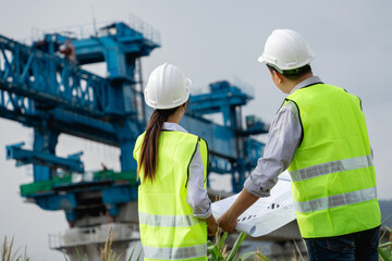Two construction workers wearing safety gear standing in front of a large blue crane.