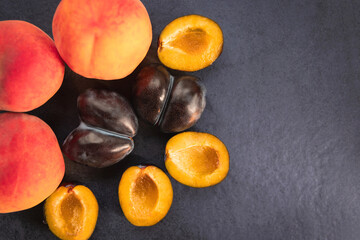 Fresh peaches and plums on a dark slate background. A combination of whole and sliced plums is arranged on a dark slate background. Top view. Free copy space.