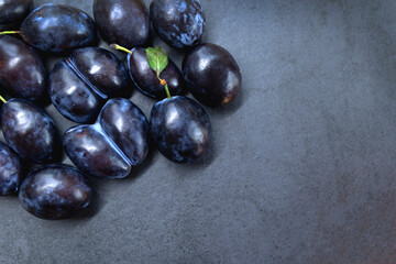 Fresh ripe plums on a dark slate background. A cluster of fresh ripe plums is displayed on a dark slate background, with one plum featuring a small green leaf. Top view. Copy space.