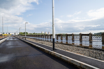 Fototapeta premium An image depicts a tranquil road accompanied by a sturdy fence, all set against the stunning backdrop of a serene body of water. This picturesque scene evokes a sense of peace