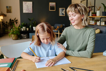 Blonde mom supporting her daughter while she writing essay for school