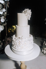 Big tall decorated wedding white three-tier cake stands on wooden table stand. Food photo, sweet dessert.