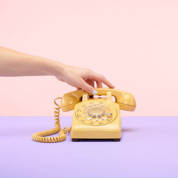 Yellow Retro Vintage Rotary Phone on Purple and Pink Tablet Top Set Still Life with Hand Reaching and Holding