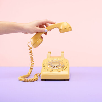 Yellow Retro Vintage Rotary Phone on Purple and Pink Tablet Top Set Still Life with Hand Reaching and Holding