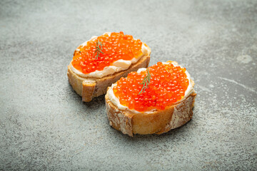 Two caviar toasts baguette canape with butter and red salmon caviar top view on grey concrete background, festive luxury delicacy and appetizer.