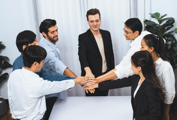 Group of diverse office worker join hand together in office room symbolize business synergy and strong productive teamwork in workplace. Cooperation and unity between business employee. Prudent