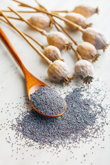 Dry poppy head and poppy seed in spoon on kitchen table.