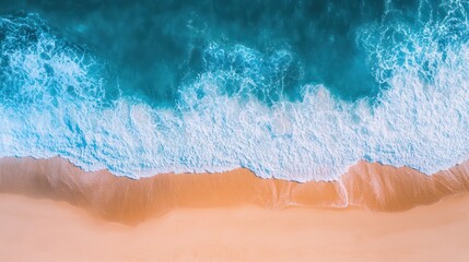 Fototapeta premium Aerial view of gentle ocean waves lapping the soft, golden sandy shore under bright sunlight.