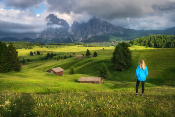 Girl on the field with yellow flowers and green grass in beautiful alpine mountain valley at sunset...
