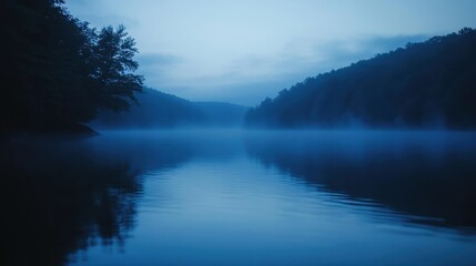 Fototapeta premium A serene landscape at dawn with mist over a calm lake and forested hills.