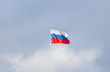 Russian tricolor flag waving in the wind against a blue sky.