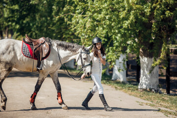 A young equestrian is gently guiding a beautiful white horse in a sunny, charming stable