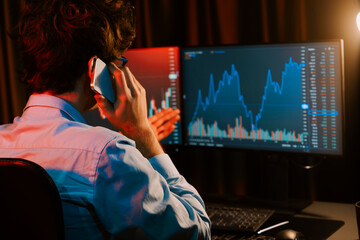 Young investor stock trader calling with broker to invest earning highest profit on current market graph online in real time at neon light modern office, monitor showing investment exchange. Gusher.