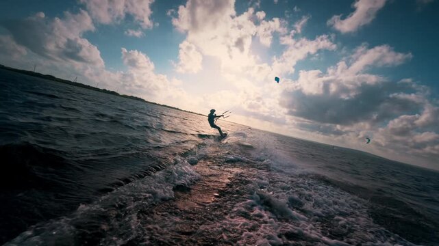 Kite surfer against beautiful cloudy sunset at sea. Slow motion of professional male kiteboarder moving fast on waves downwind