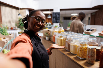 POV of African American eco store owner promoting sustainable, organic groceries. Customers shop for fresh, nutritious food in a modern supermarket. Online video call showcases eco friendly products.