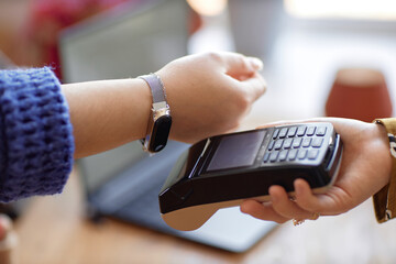 Fototapeta premium Close up on on female hand paying wireless with smartwatch and unrecognizable cashier using POS terminal at store, copy space