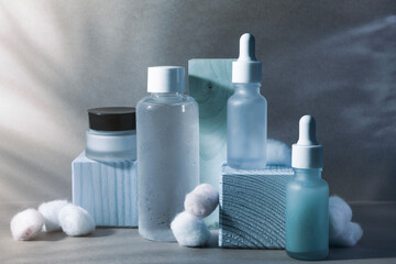 Cosmetic morning and evening still life serum, toner, cream. Dark shadow on indigo blue background with cotton flower.