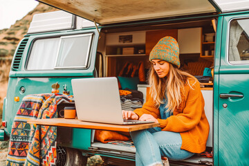 Young woman digital nomad engaging in remote work outside her vintage camper van, epitomizing the mobile, van life lifestyle
