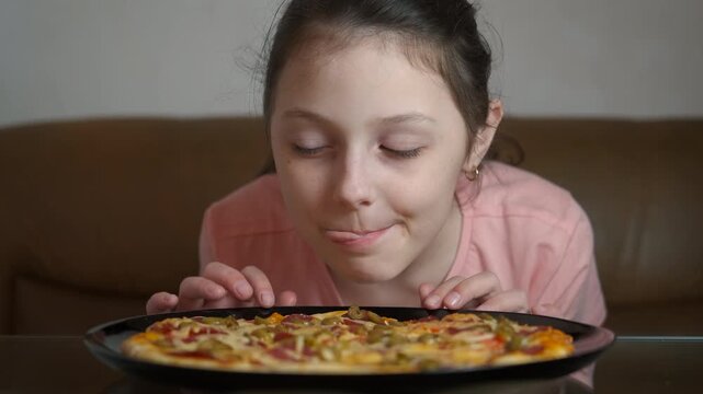 Hungry child hold tasty homemade pizza. A hangry little girl enjoy the fast-food and hold the pizza on the table.