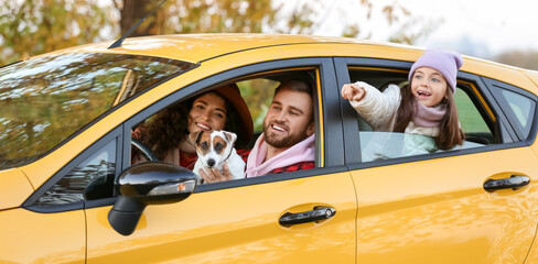 Parents with little daughter and cute dog sitting in yellow car