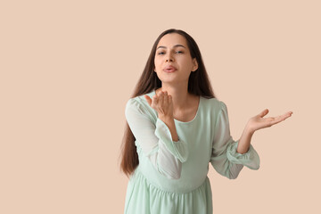 Obraz premium Happy young woman blowing kiss on beige background