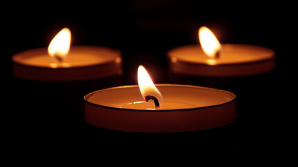 Three lit tealight candles in the darkness, emitting a warm and serene glow, creating a peaceful and calming atmosphere.