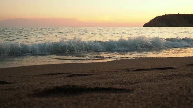 Waves gently lap at shore during stunning sunset over ocean. Golden sunlight reflects off waves as they roll onto shore, creating tranquil atmosphere at sunset by sea. Montenegro summer Canj