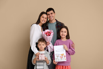 Couple and children greeting their mother with Mothers Day with bouquet of flowers, drawing and gift near beige wall