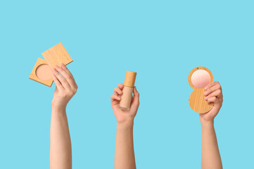 Female hands with highlighter, foundation and powder on blue background